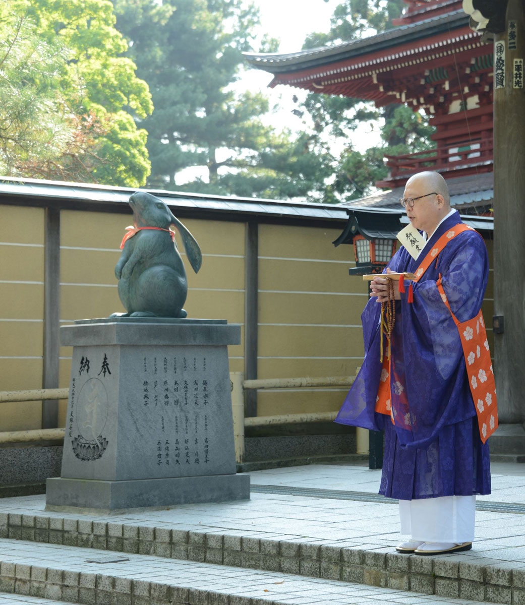 The usually stern priest looks gentle when photographed with the rabbit statue.